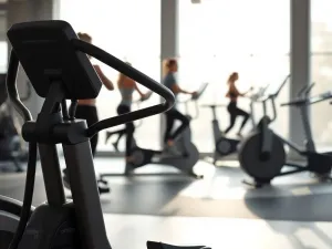 Osoba na macie dotyka jednocześnie kettla i hantla, symbolicznie wybierając sprzęt do domowego treningu.